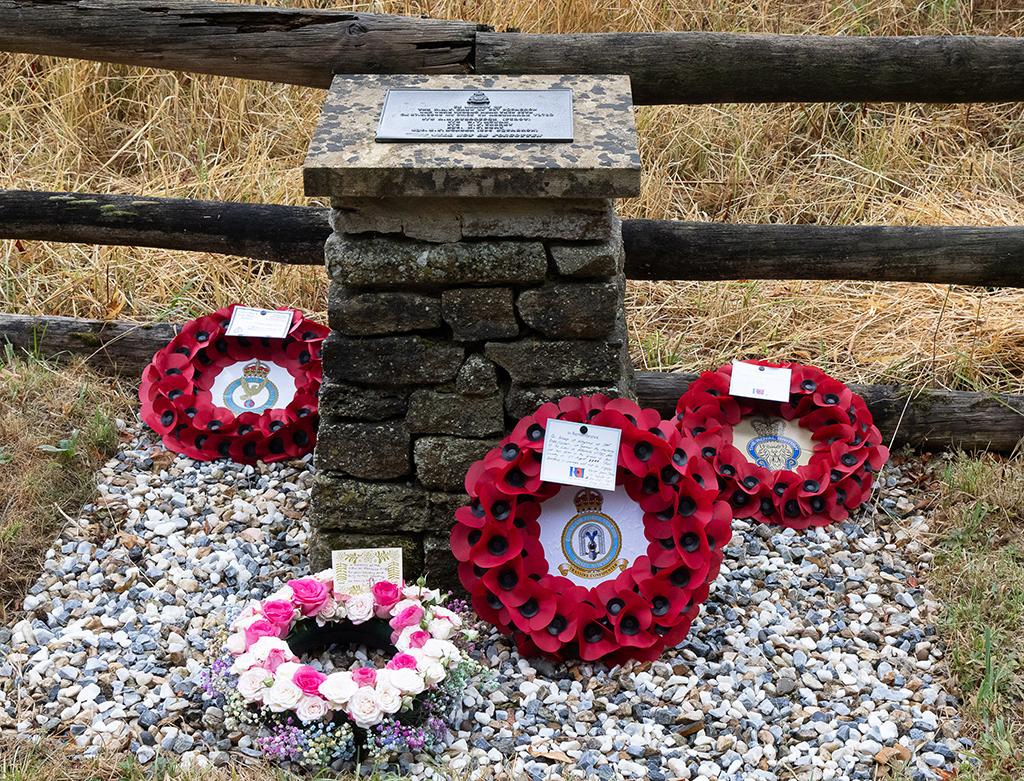 The memorial for the crew, with the plaque atop showing the names of the dead airmen, Flight Sergeant Alan Henry Busbridge, Flight Sergeant Bernard Vincent Mowan, Flight Sergeant William Frederick Insley, Sergeant Kenneth James Shay, Sergeant Edgar Frederick Bonser. The base of the memorial is surrounded with poppy and flower wreaths.